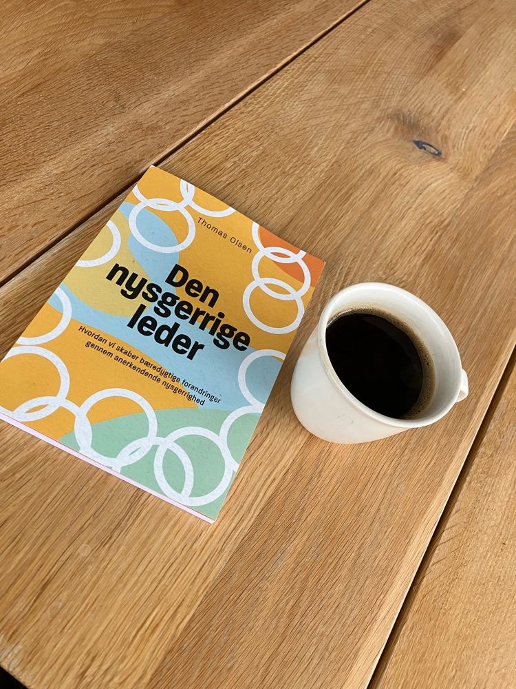 Bogen Den nysgerrige leder på et egetræsbord ved siden af en kop kaffe